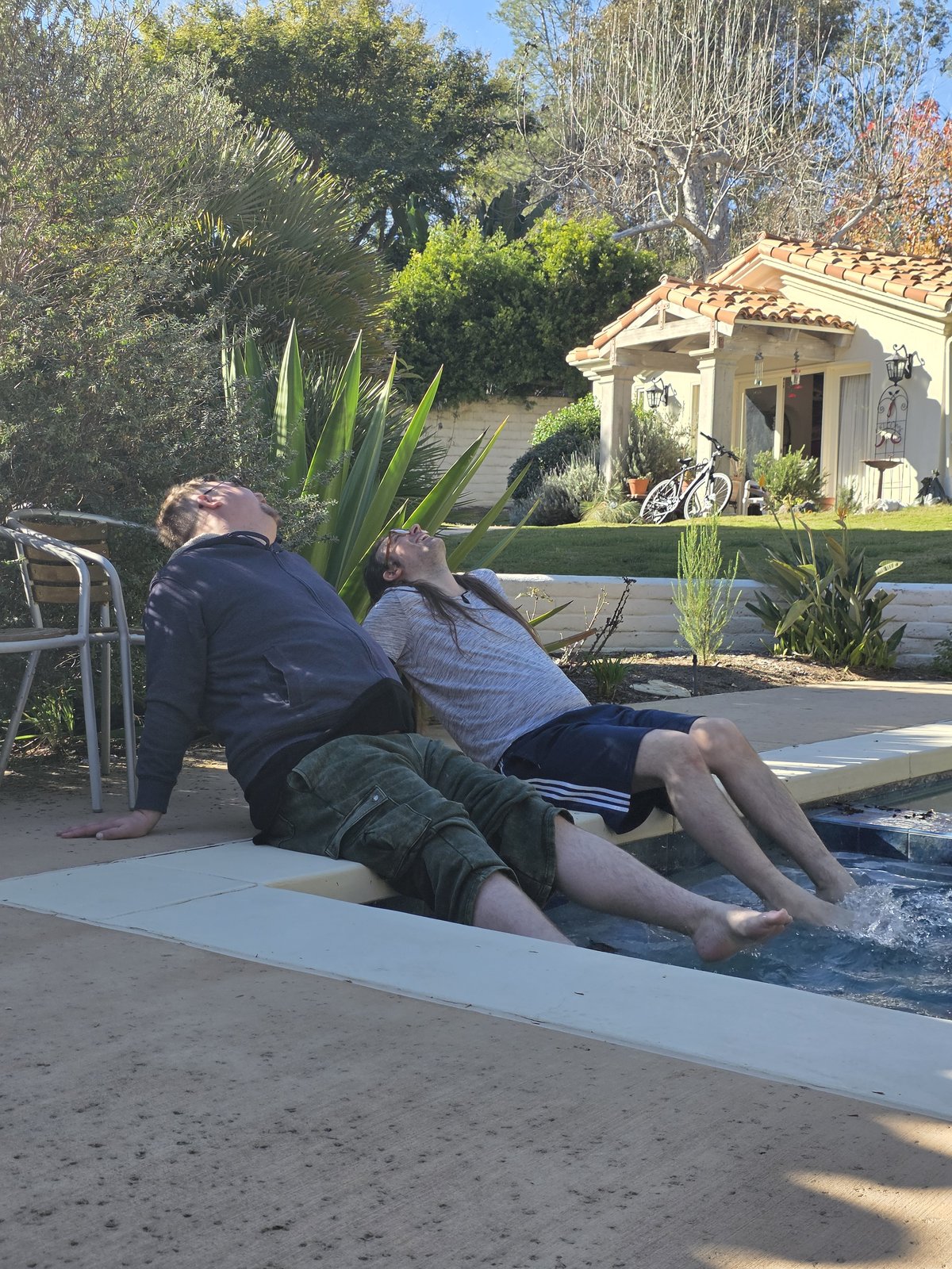 Goose and Squirrelybass collapsed back-to-back at the edge of a pool, feet in the water, heads thrown back